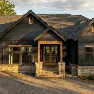 Modern dark-gray house with wood garage, stone porch and warm sunset light among trees. Jasper, GA Reynard Architectural Designs