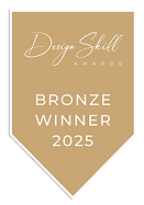 A muted bronze, banner-shaped award badge featuring white text. The top reads "Design Skill Awards" with "Design Skill" written in a cursive script and "Awards" in small capital letters. The bottom section reads "BRONZE WINNER 2025" in bold, sans-serif capital letters. Reynard Custom Homes Architecture