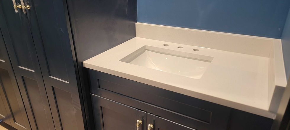 Navy blue cabinets with brass handles beside a white countertop and sink against a blue wall, creating a modern bathroom setting.