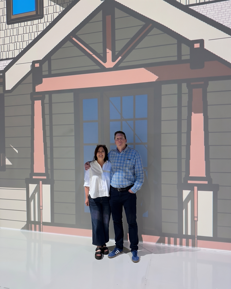 Couple posing happily in front of a house graphic backdrop with muted colors. They wear casual outfits; the man wears a checked shirt. Reynard Architectural Designs touring Walk Your Plans Atlanta in Roswell, GA