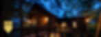 Rustic modern cabin lit at dusk among trees, with an Atlanta Home Georgia Design Awards Gold Winner 2023 badge. designed by James Knight of Reynard Architectural Designs