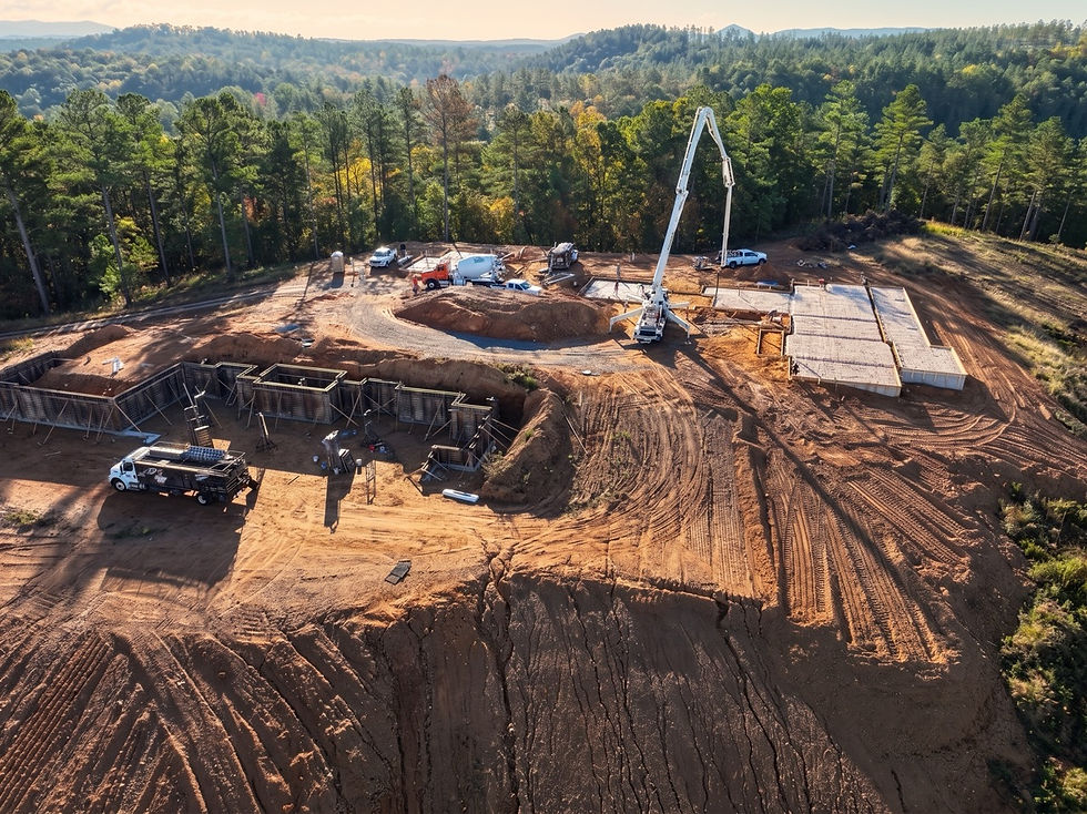 Aerial view of a forested construction site with concrete foundations, a pump truck, and dirt roads under warm sunlight. When designing a custom home from the ground up, the land itself should shape every major decision. This was exactly the case for a recently designed multi-generational compound in Talking Rock, Georgia—one of the most layered and site-driven projects in the Reynard Architectural Designs portfolio.
