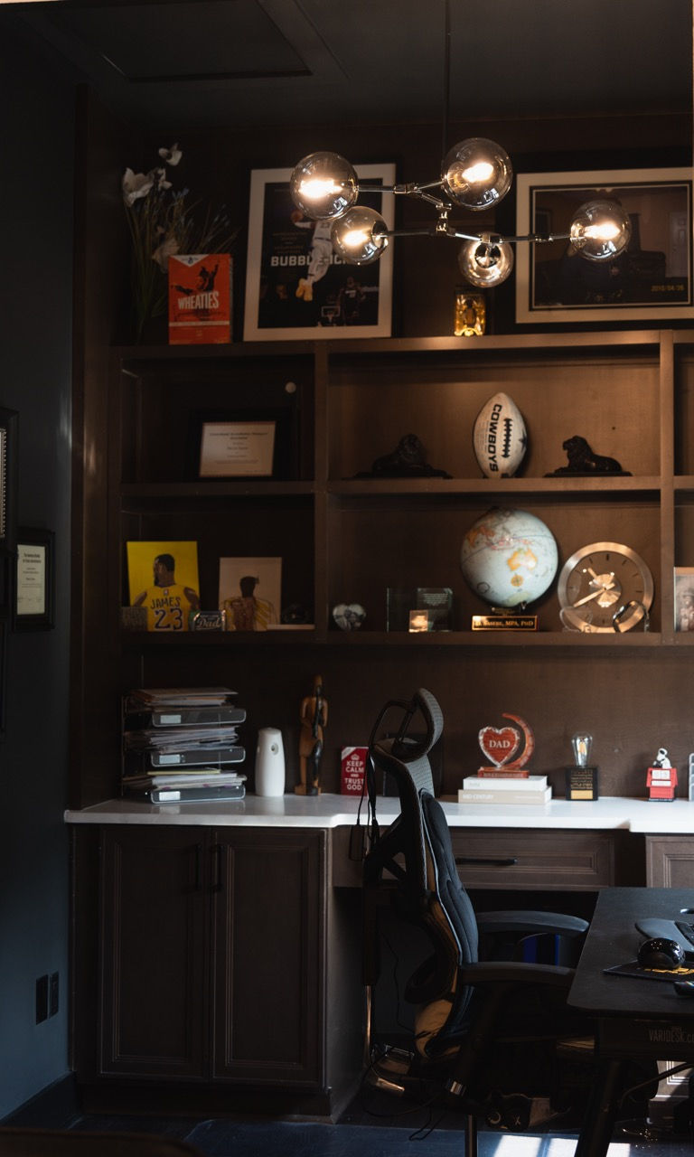 A moody and sophisticated home office featuring floor-to-ceiling dark wood cabinetry, integrated she