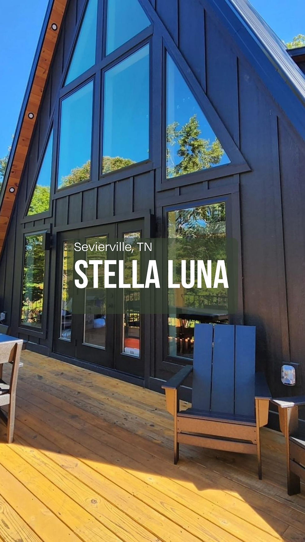 A-frame cabin with large windows, black exterior, and wooden deck. Text reads "Sevierville, TN Stella Luna." Bright and sunny atmosphere. Reynard Architectural Designs. Reynard Custom Homes.