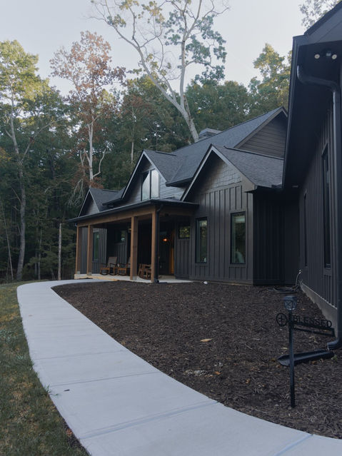 Exterior of the dark-painted Redfield home in Jasper, GA, showing a concrete walkway leading to a covered front porch with natural wood columns. Custom home designed by Reynard Architectural Designs