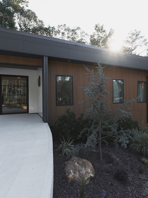 Exterior view of a modern house highlighting vertical wood siding, a dark trim roofline, large black-framed windows, and manicured landscaping with ornamental grasses and rocks. Architecture by James Knight Photo by Kalyn Kight Reynard Architectural Designs