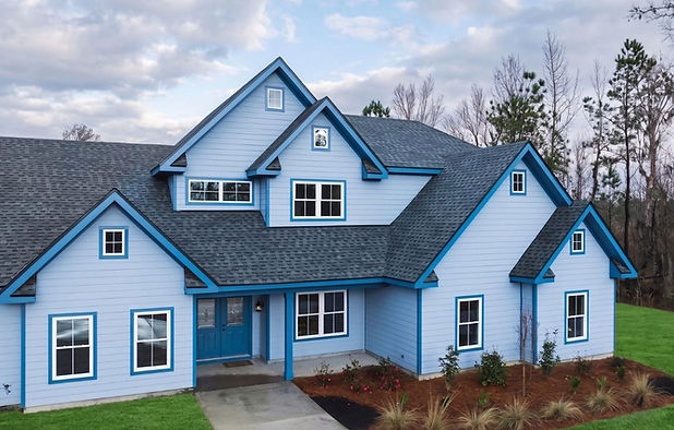 A high-angle shot of a large suburban home featuring light blue horizontal siding with dark blue trim along the roofs, windows, and front doors, surrounded by a manicured green lawn.