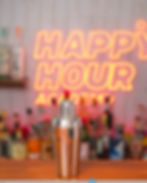 a cocktail shaker sitting atop a bar with happy hour academy's neon sign in the background
