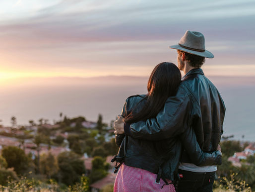 Romantic couple embraces while watching the sun set over the ocean, creating a tranquil moment.