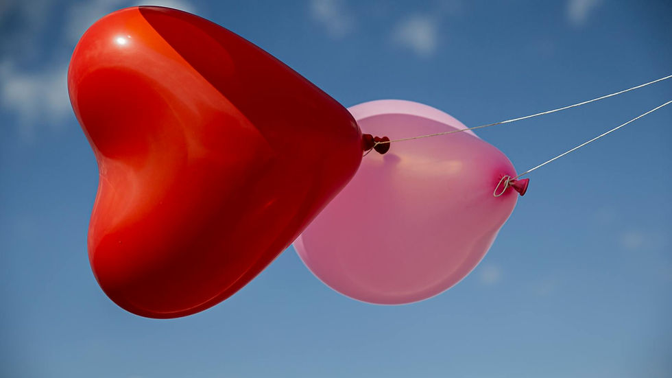 Red heart-shaped balloon and pink round balloon floating against a clear blue sky.