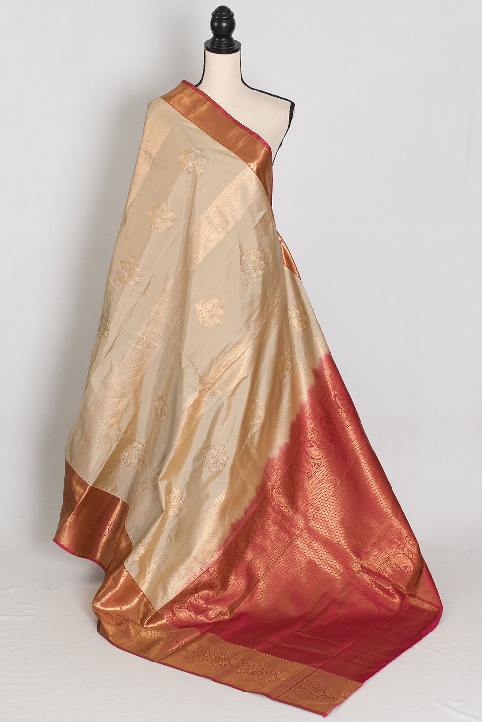 Mud white semi silk Kanjivaram saree with a brick red contrast skirt border and gold zari details draped on a mannequin.
