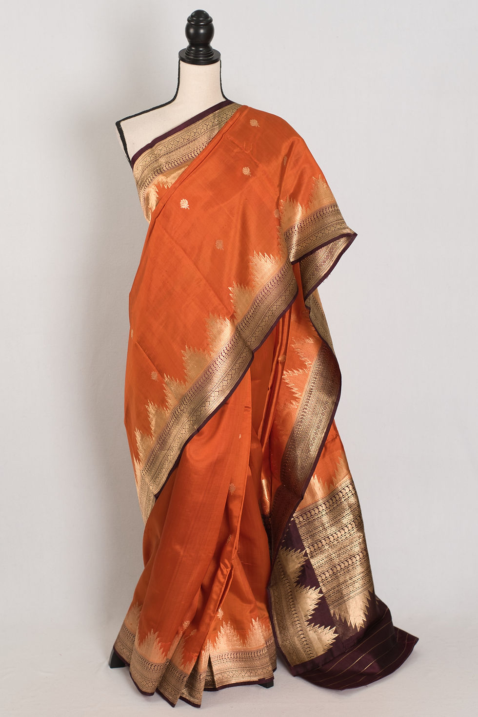 Bina rust orange and coffee brown handwoven Banarasi silk saree with golden zari temple border on a mannequin.