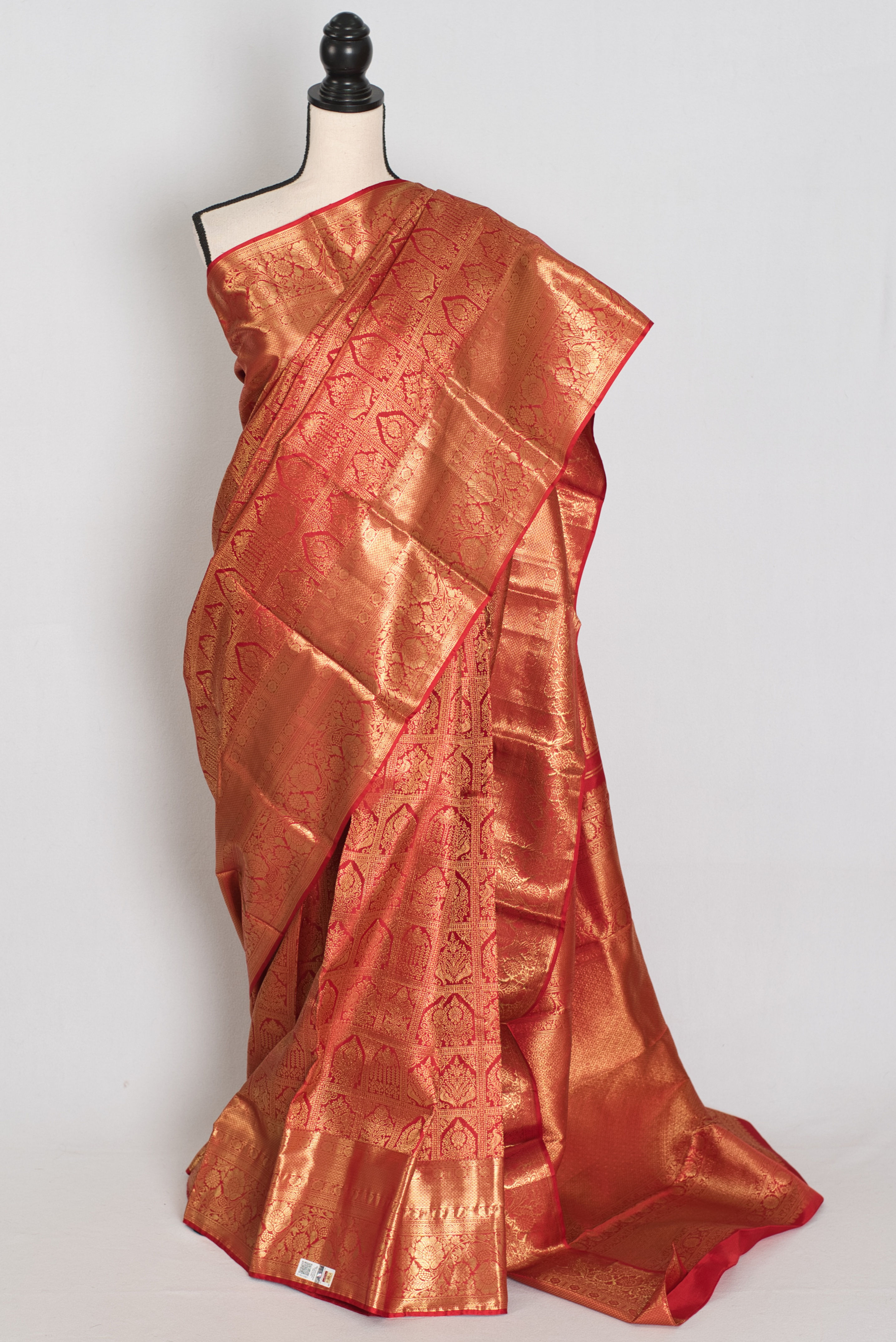 Premium red and gold bridal Kanjivaram silk saree with heavy gold zari brocade patterns draped on a mannequin.