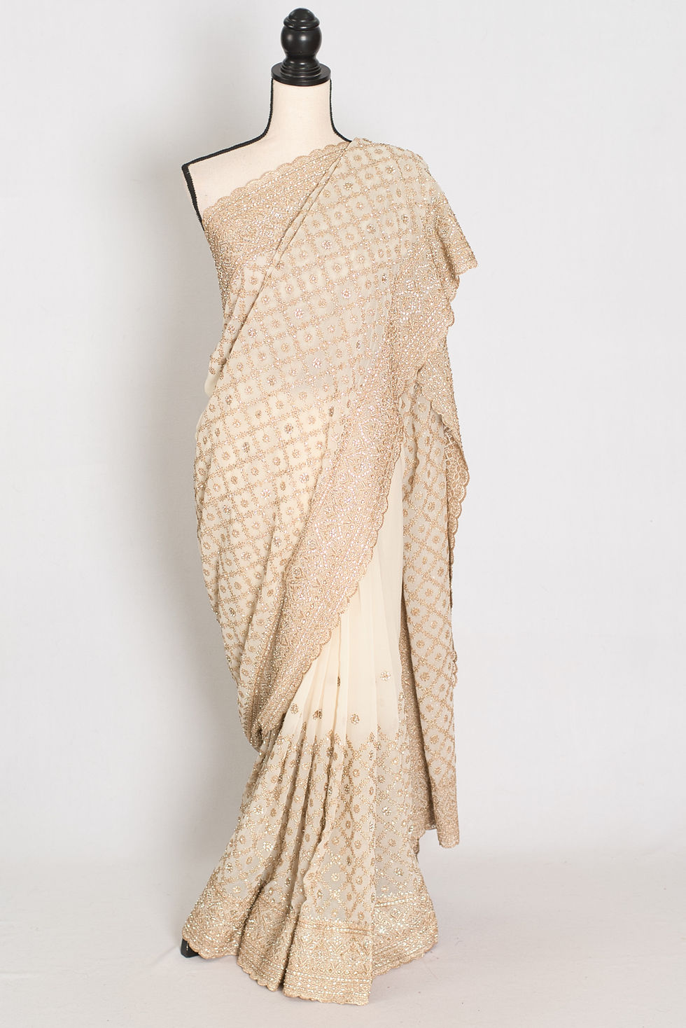 Cream and gold georgette wedding saree draped on a mannequin showing its fluid texture, scalloped borders, and heavy gold zar