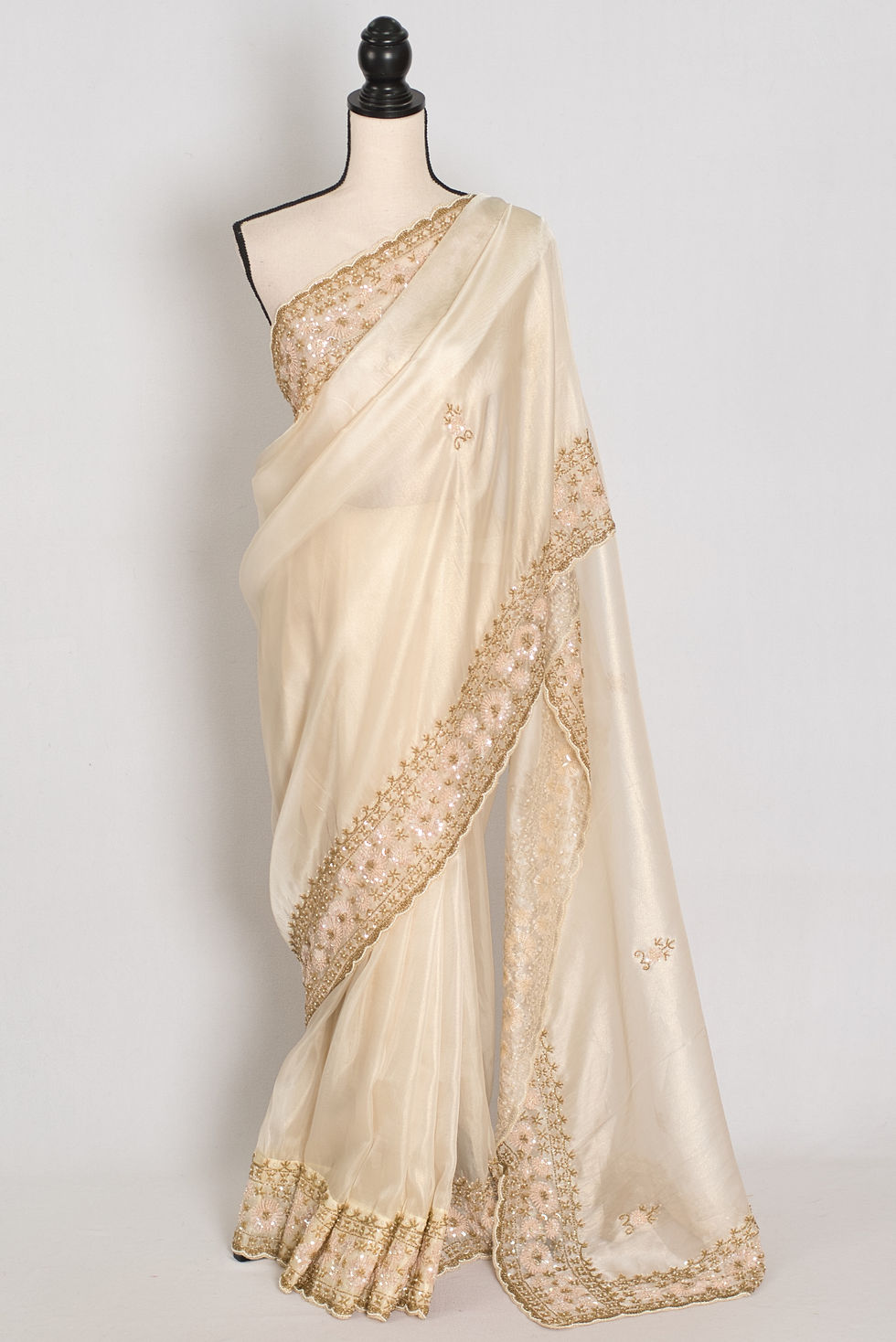Front full-length view of the cream and gold soft tissue partywear saree draped on a mannequin.