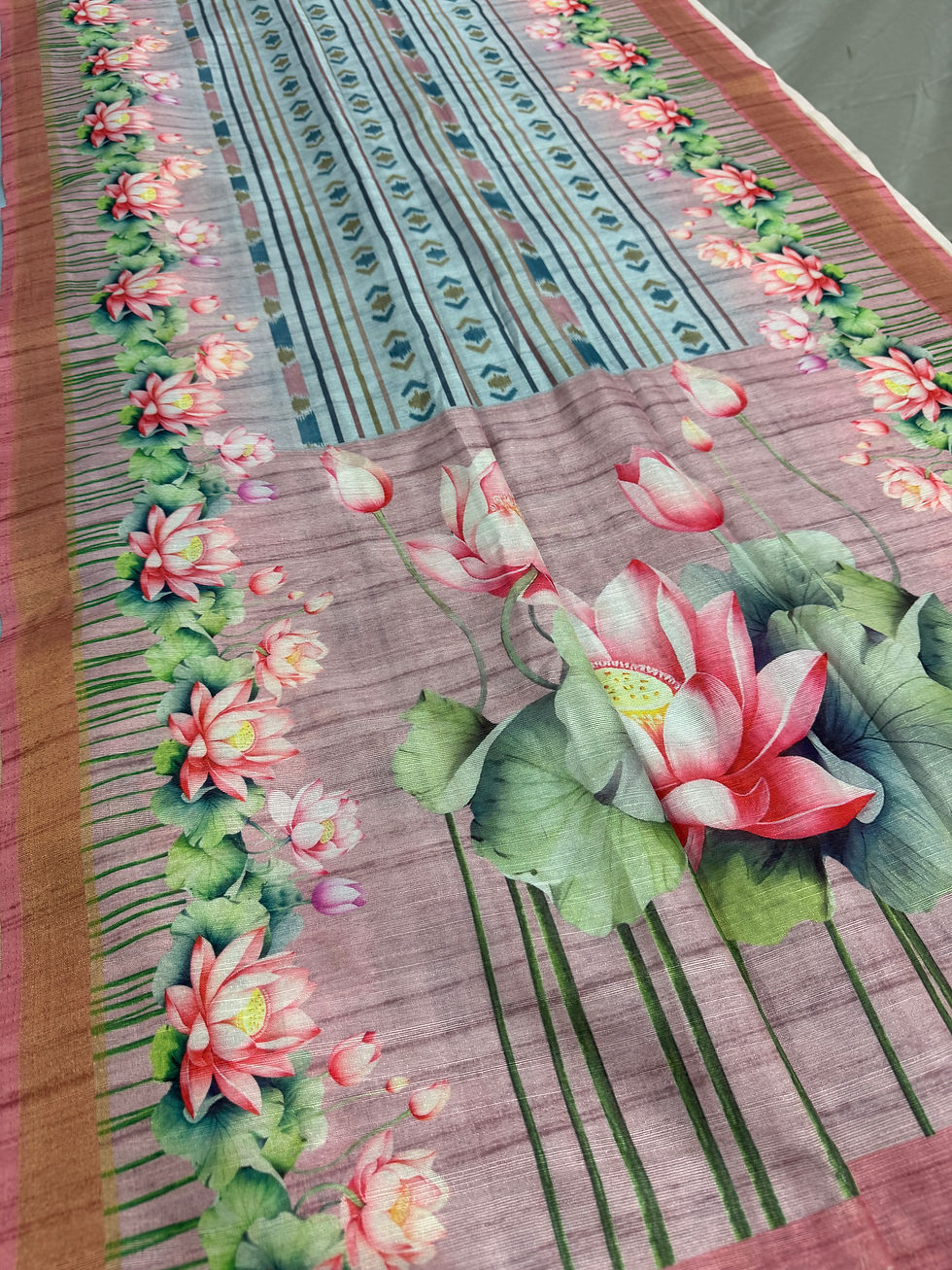 Sky blue semi tussar saree with pink lotus prints, mauve ikkat patterns, and matching mauve blouse piece.