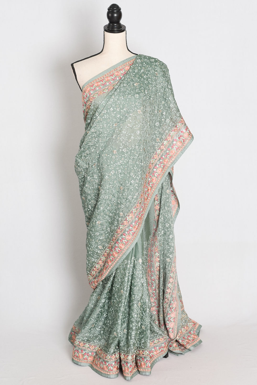 teal green crushed georgette saree with all-over intricate floral machine embroidery and pink border on a mannequin.