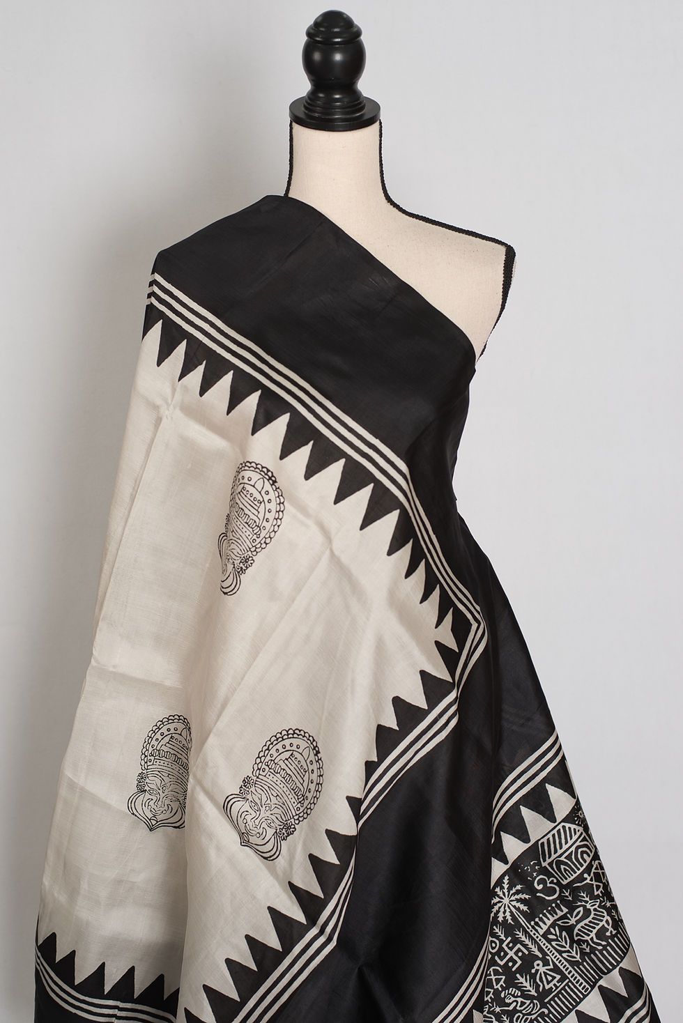 Thumbnail: Off-white and black Murshidabad silk saree with Kalamkari-style mask prints and a geometric temple border on a mannequin.
