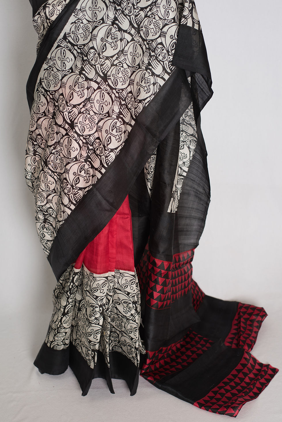 Thumbnail: Black and red half and half Murshidabad silk saree with hand block printed tribal face motifs draped on a mannequin.