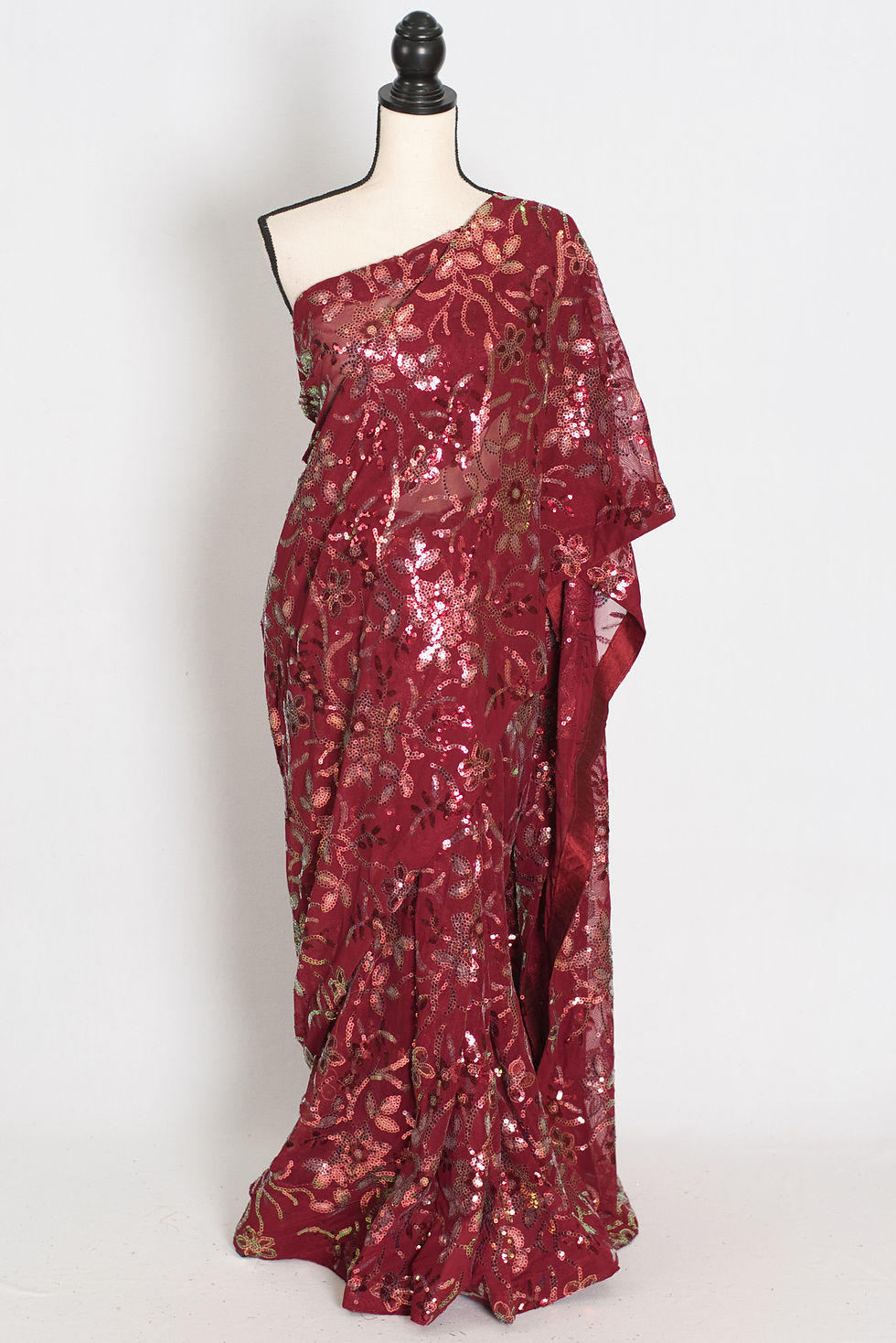 Brownish maroon partywear sequin saree draped on a mannequin showcasing its fluid silhouette and all-over Bollywood-style flo
