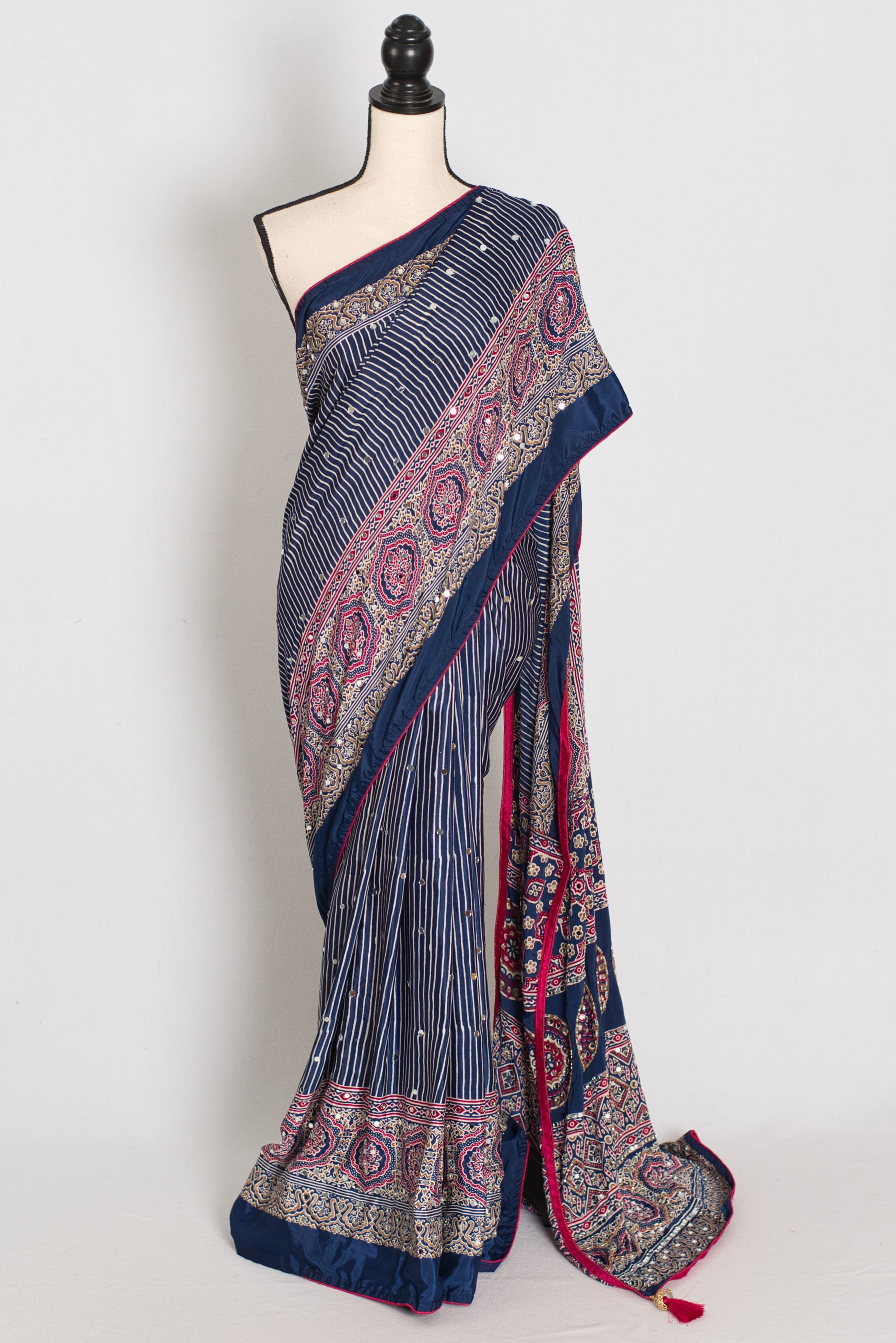 Blue Ajrakh party wear saree draped on a mannequin, showcasing its slimming vertical stripe pattern body with all-over mirror