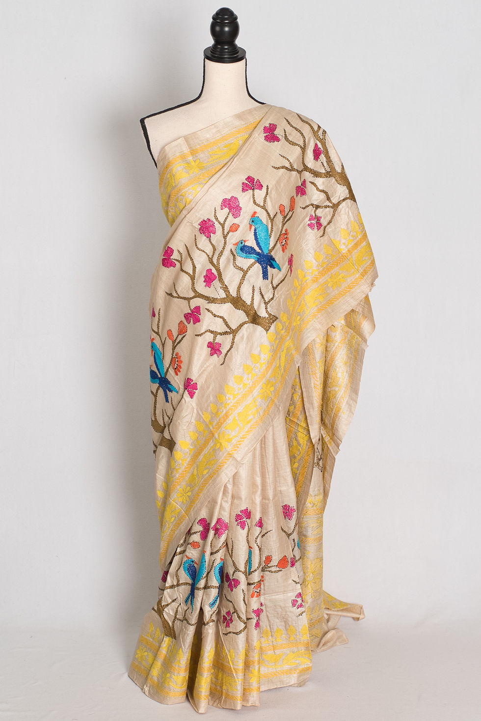 Tussar silk saree in beige and yellow featuring hand-embroidered blue birds on flowering branches draped on a mannequin.