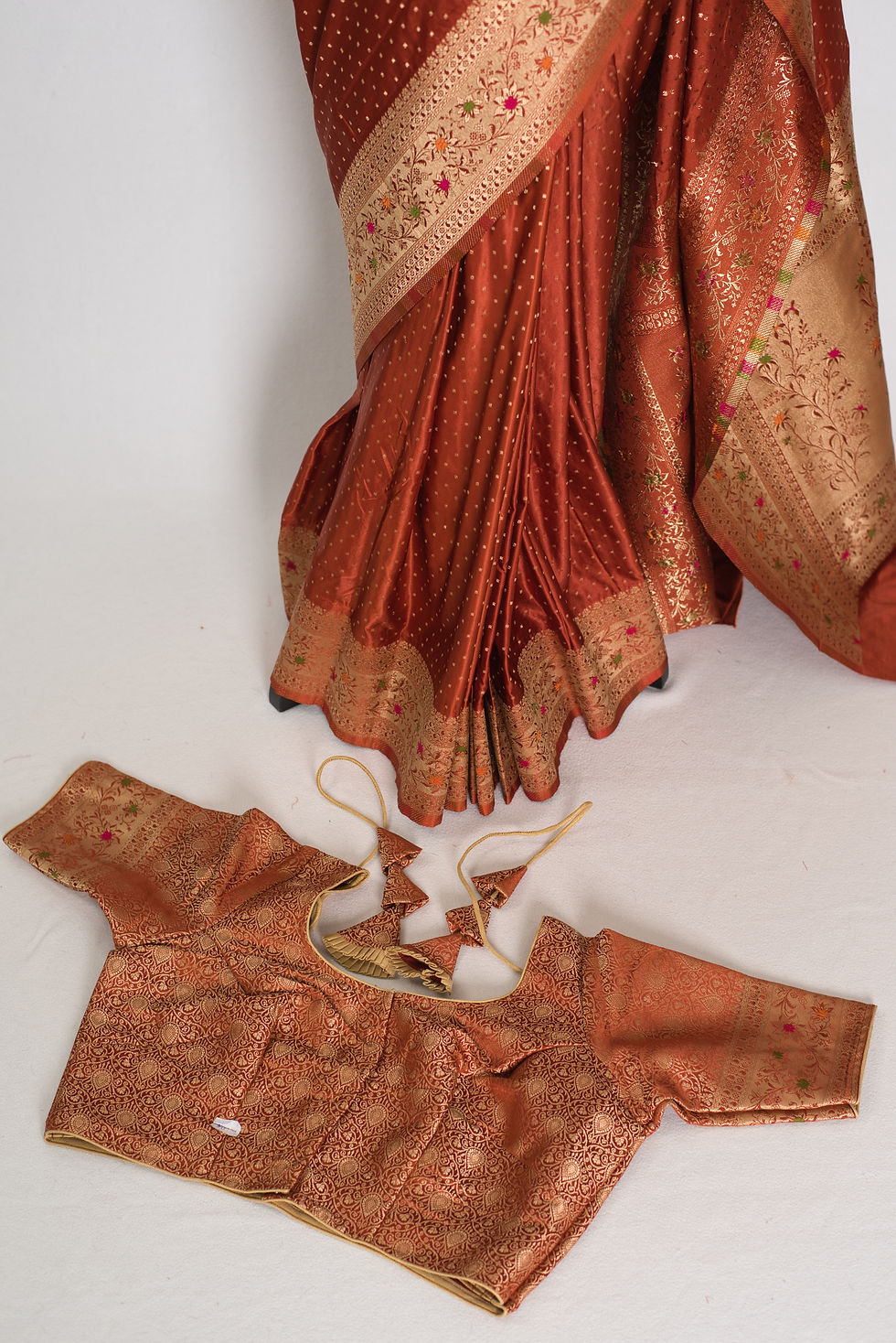 Rust orange semi mashru Banarasi saree draped on a mannequin displaying woven floral border.