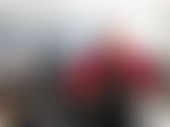 Jeni Wheeler, a member of World Central Kitchen, smiling and wearing a red chef jacket and a black apron with the World Central Kitchen logo, standing in a busy kitchen with other volunteers in the background.