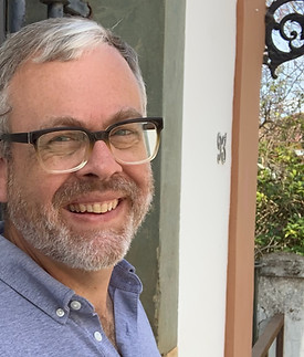 Kevin's face smiles, he has salt-and-pepper hair and beard. He wears a blue polo shirt and black-framed glasses.