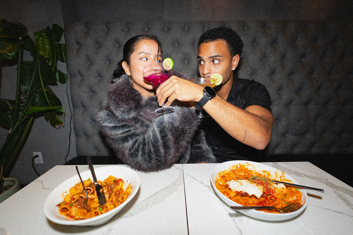 Two diners toast cocktails over plates of pasta, photographed by Archive Studios