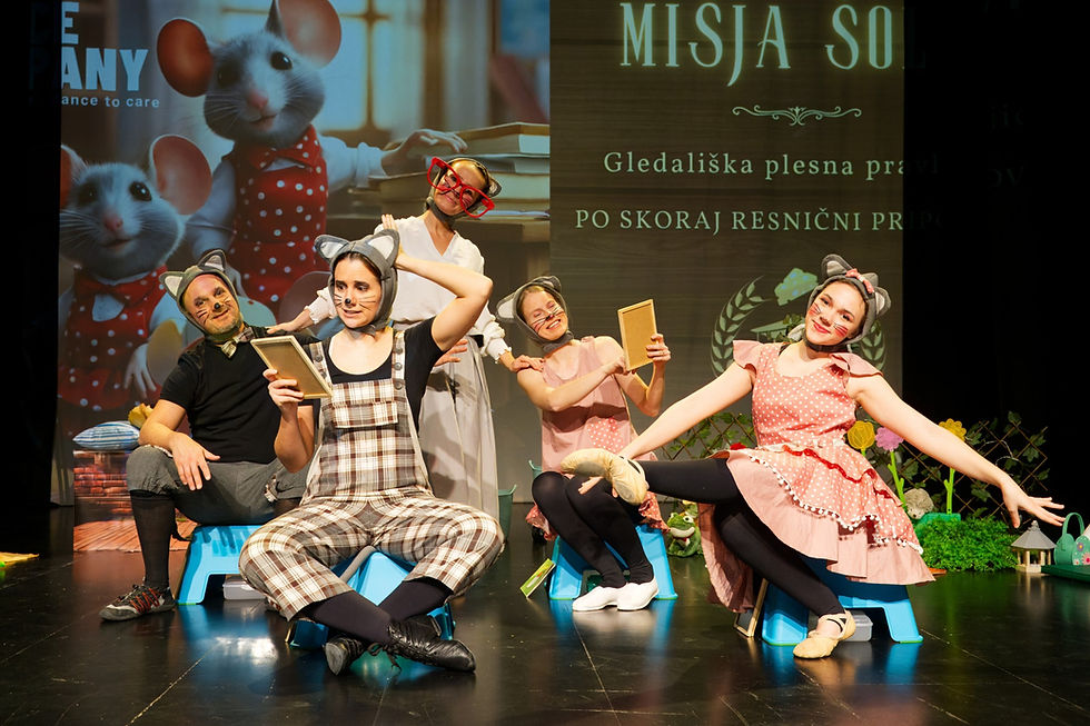 Ljudje v oblačilih miši pozirajo na odru; ena drži tablo. Veselo ozračje, zadaj je plakat s podganami in besedilom "MISJA SOL".