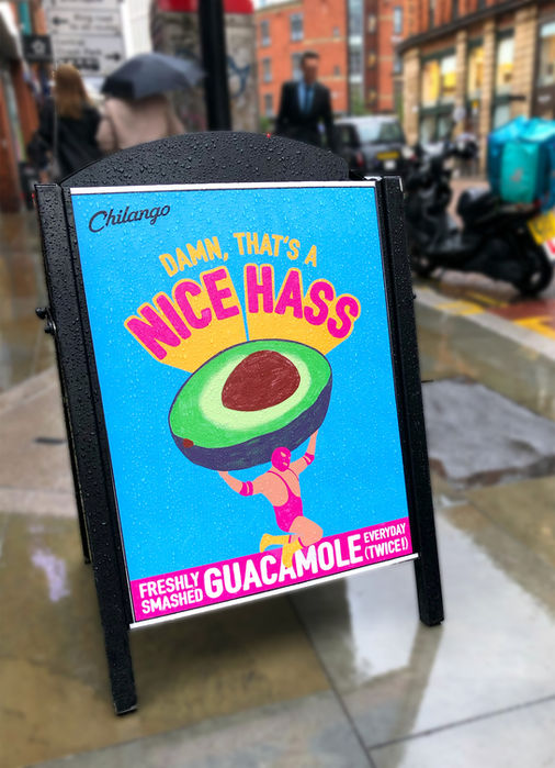 an a-board on oxford street in manchester, with an illustration of a mexican wrestler holding up a giant avocado, with the title 'that's a big hass'