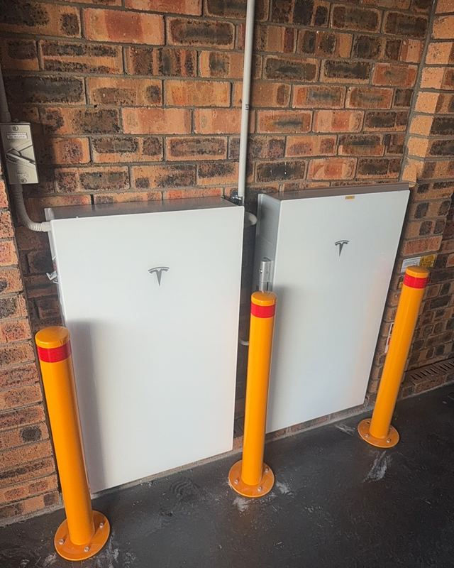 Two home batteries mounted on a brick wall with safety bollards in Mulgoa NSW