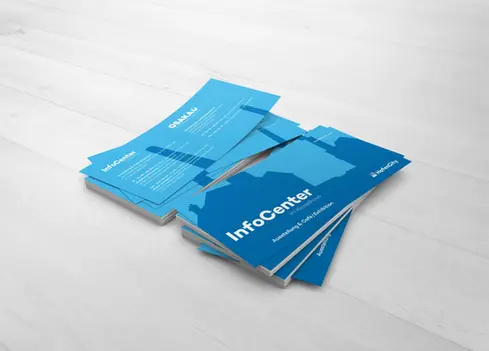 Stacked blue flyers for 'InfoCenter im Kesselhaus' and 'OSAKA' on a light-colored wooden floor. 