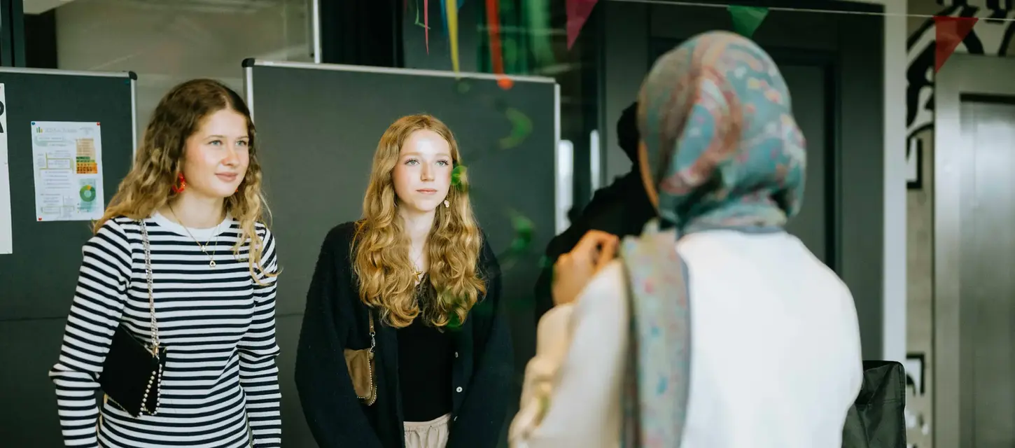 Zwei junge Frauen an Stand mit "SPENDEN" Schild interagieren mit Person.