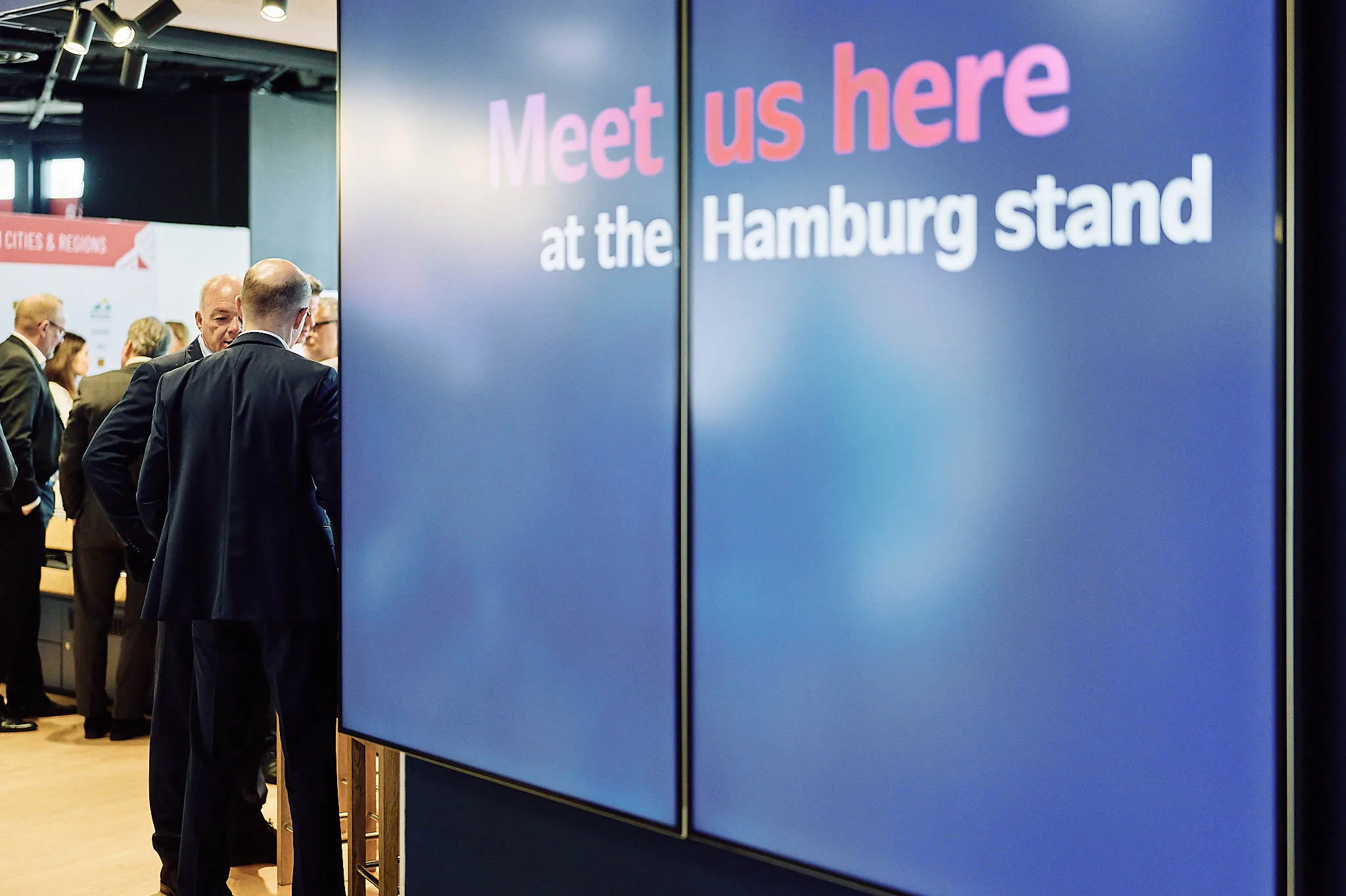 Large screen displaying 'Meet us here at the Hamburg stand'