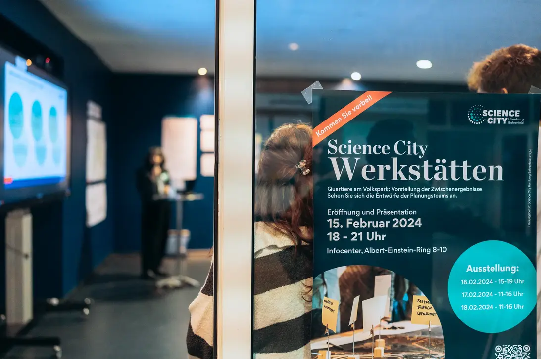 Poster for Science City workshops on glass door, person entering exhibition space with presentation screen in background
