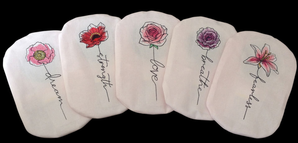 Five pink stoma bag covers embroidered with flowers on a black background.