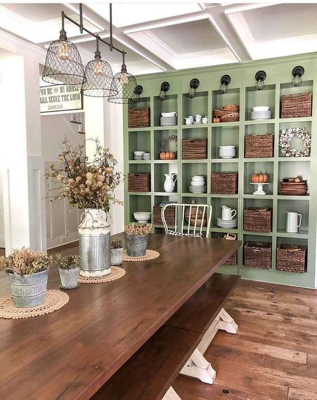 une bibliothèque ancienne peinte en vert, des murs blanc et une table de ferme en bois brut pour une cuisine cosy