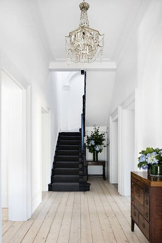 un escalier d'une maison des années 30 peint en noir profond accompagné d'une commode en bois brut pour une entrée haute en couleur