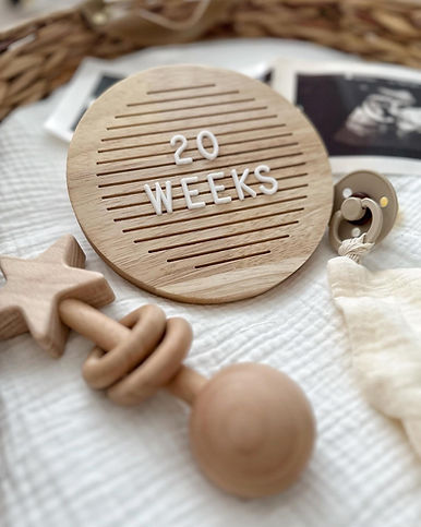 An arrangement of a baby rattle, next to a wooden letterboard announcing a pregnancy