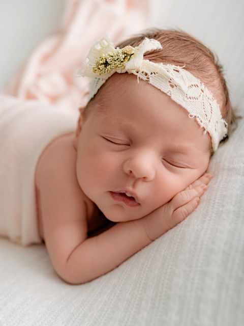 beautiful newborn baby girl sleeping in a posed position with a wrap and floral headband