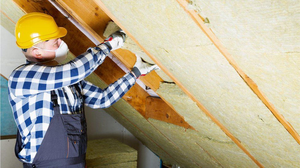 Garden room roof being insulated by man wearing a helmet and a dust mask