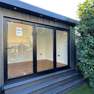 3.8m x 3m Garden Pod, with dark grey wood textured composite cladding and a 3m aluminium panel bifold door. This building also included three black composite decking steps.