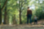 Woman and toddler walking on sunny path, trees lining way