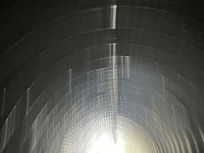 Abstract black-and-white photograph of a curved tunnel with bright light at the far end.