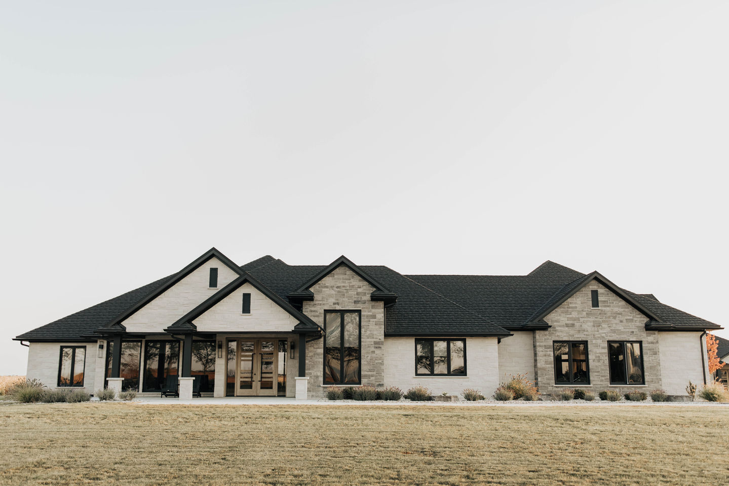Modern farmhouse with black roof and neutral stone facade, surrounded by lush, low-maintenance garden design by WaveScapes.