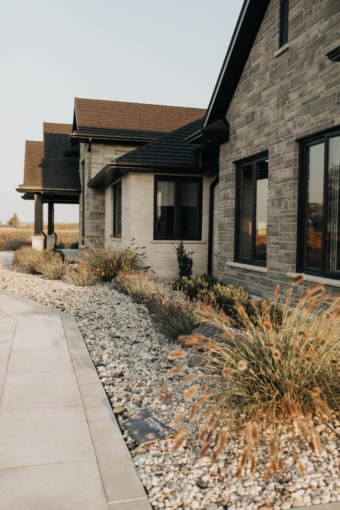 Modern landscape design by WaveScapes Design featuring ornamental fountain grass and gravel edging that create a clean, low-maintenance curb appeal in natural evening light.
