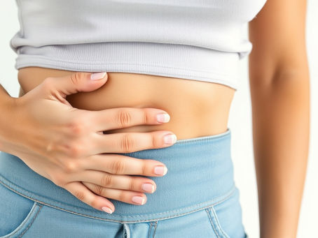 Person wearing a white crop top and blue jeans touching their abdomen. The background is light, and the mood is focused on physical sensation.