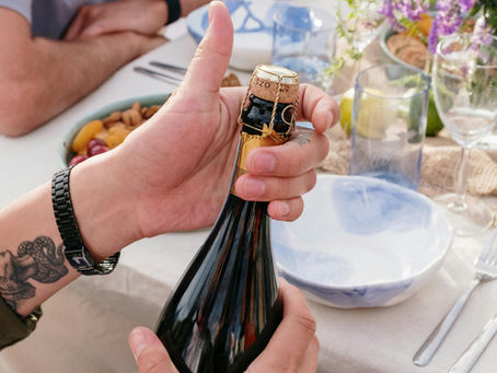 Hands open a grower champagne bottle at an outdoor brunch table